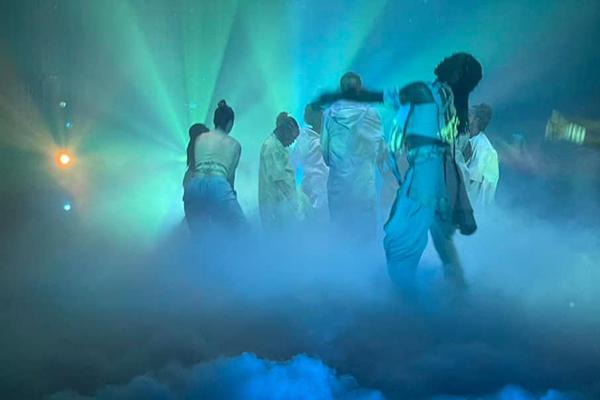 Dancers dressed in white performing on a foggy stage with blue and green lights