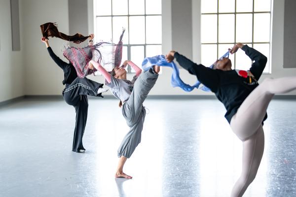 3 dancers leaning back with one leg extended waving scarves in a studio
