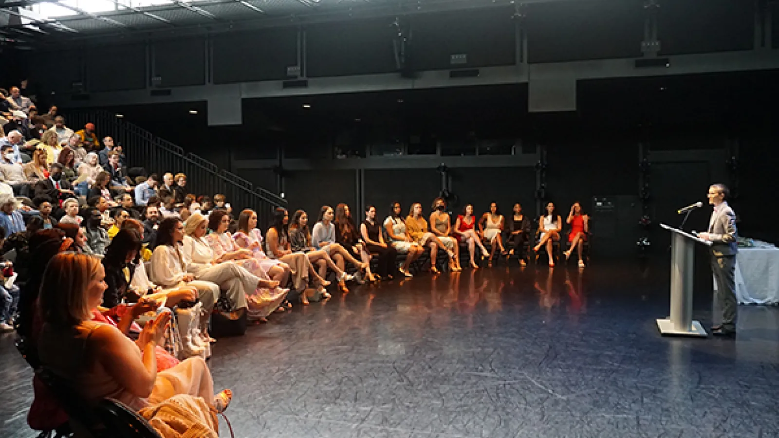 Students seated on stage listening to a speaker