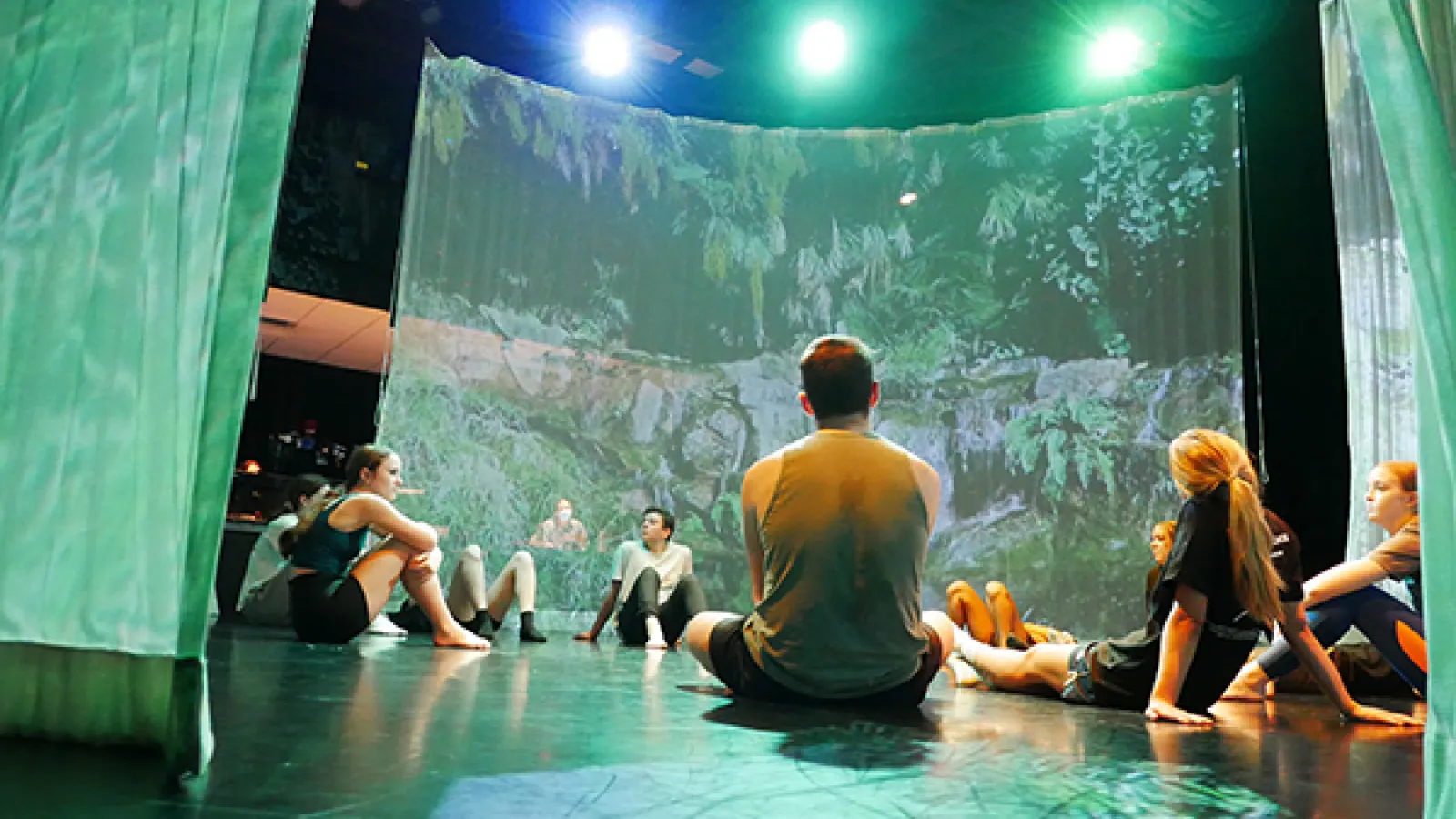 Students sitting on floor with a screen and blue and green lights in background