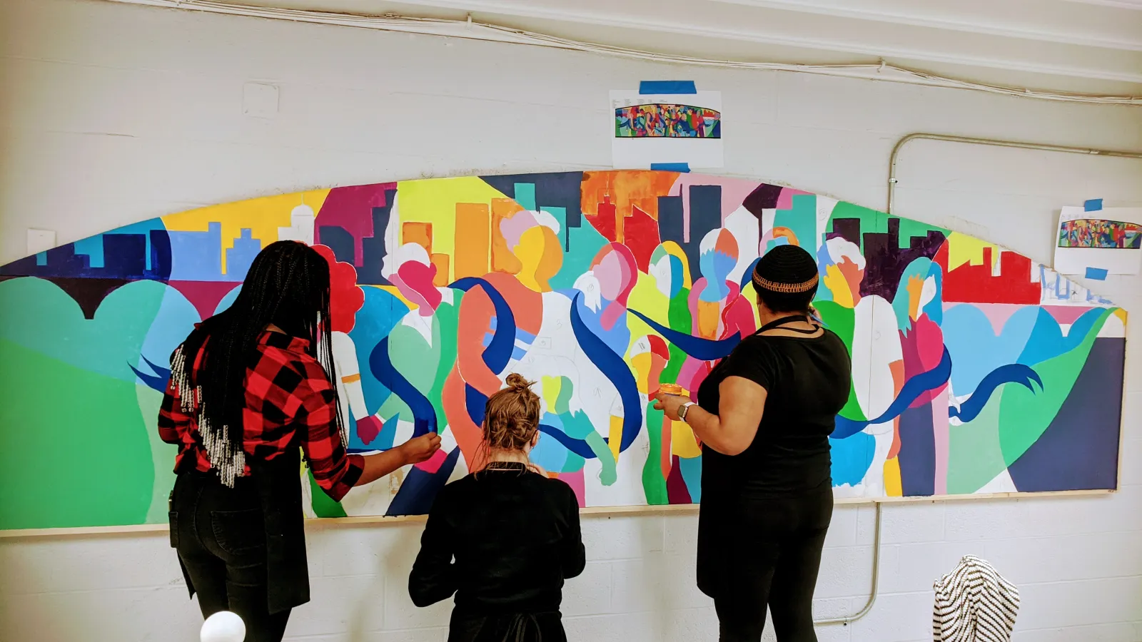 3 people painting a mural on a wall 