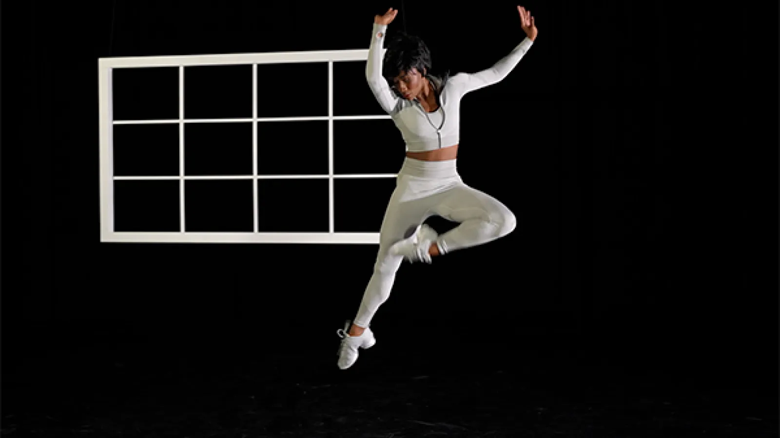 Dancer dressed in white leaping in front of white window frame