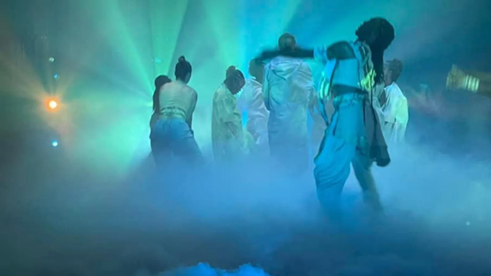 Dancers dressed in white performing on a foggy stage with blue and green lights