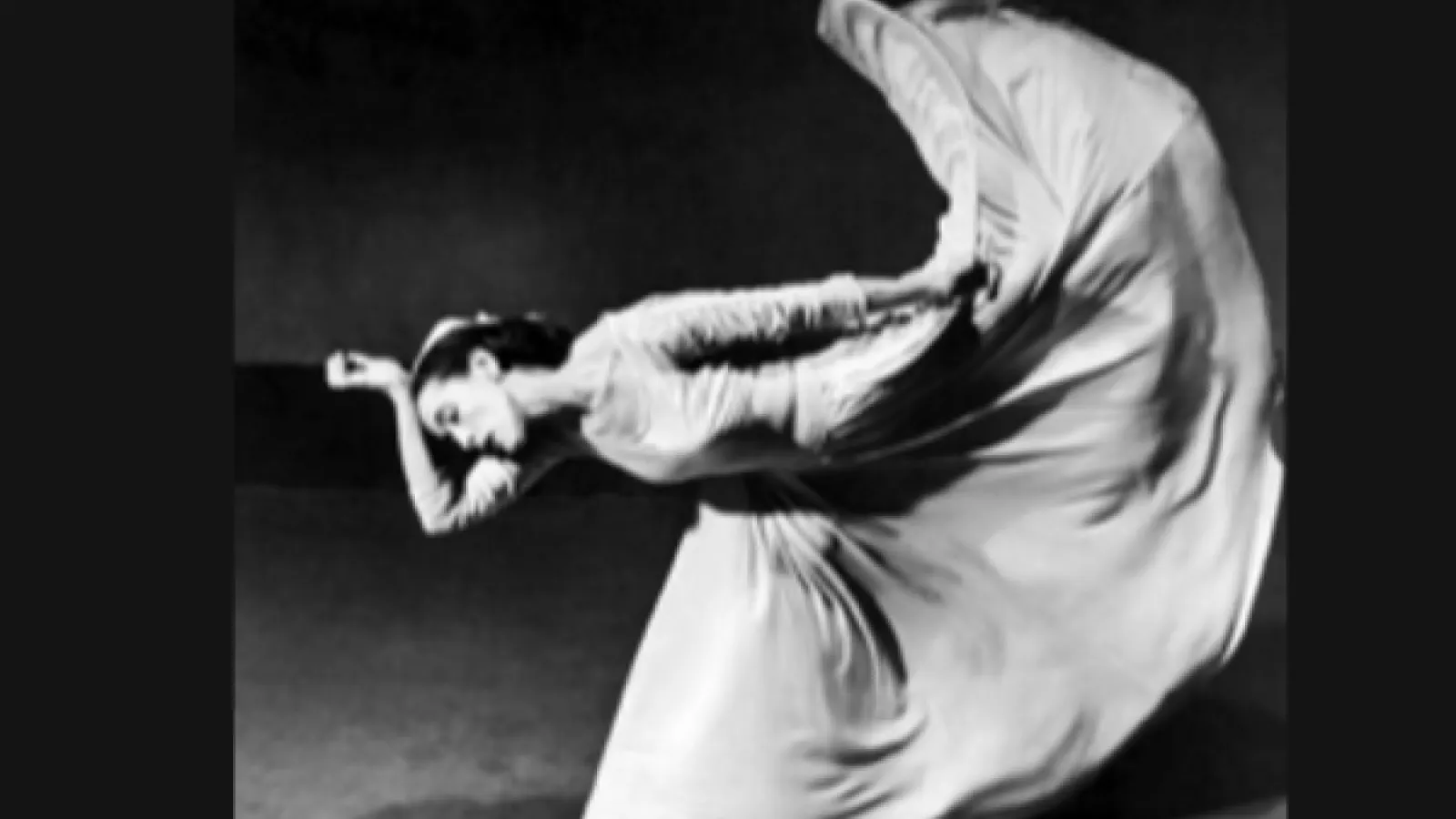 black and white photo of dancer in long white dress with one hand on her head and one leg lifted