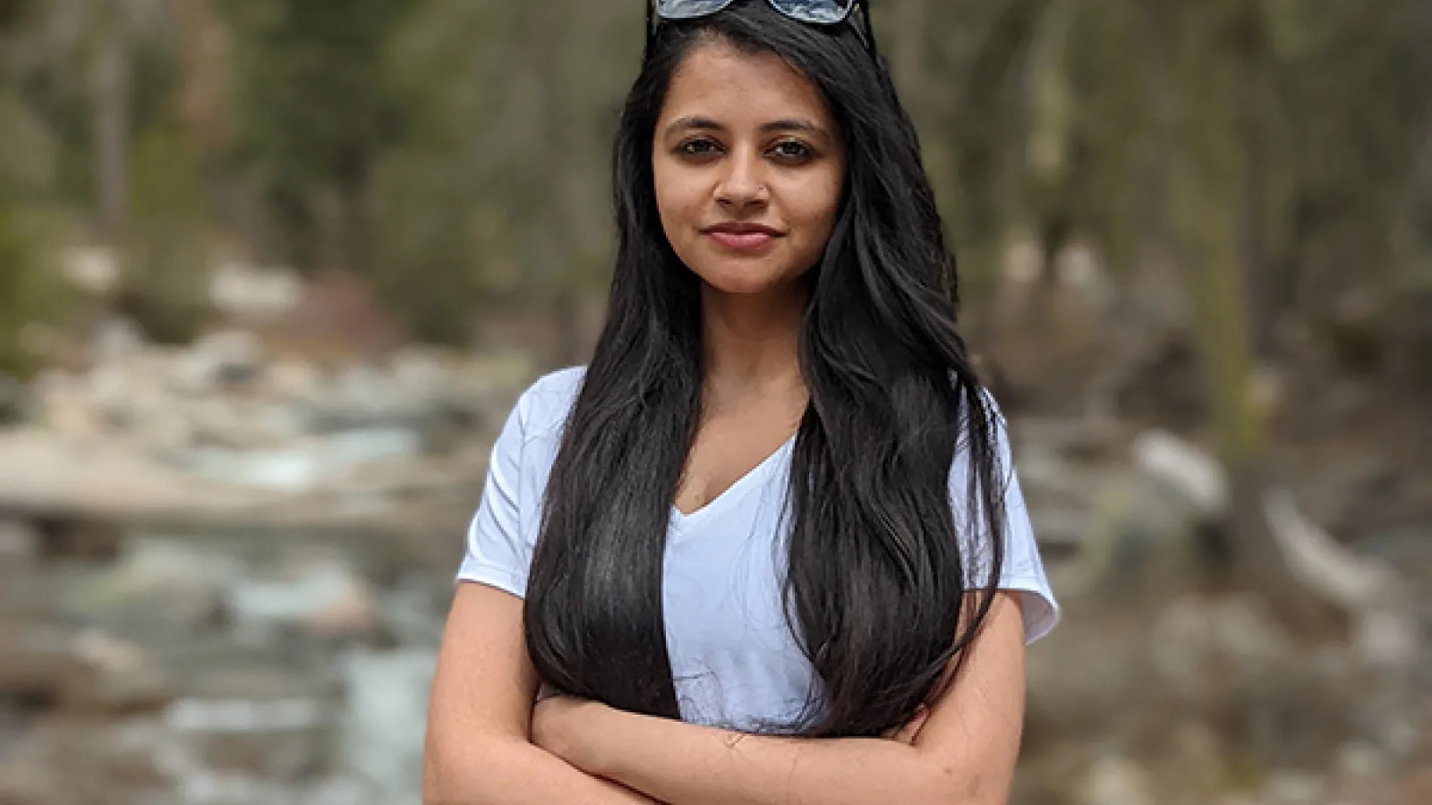Person with long black hair standing in front of woods