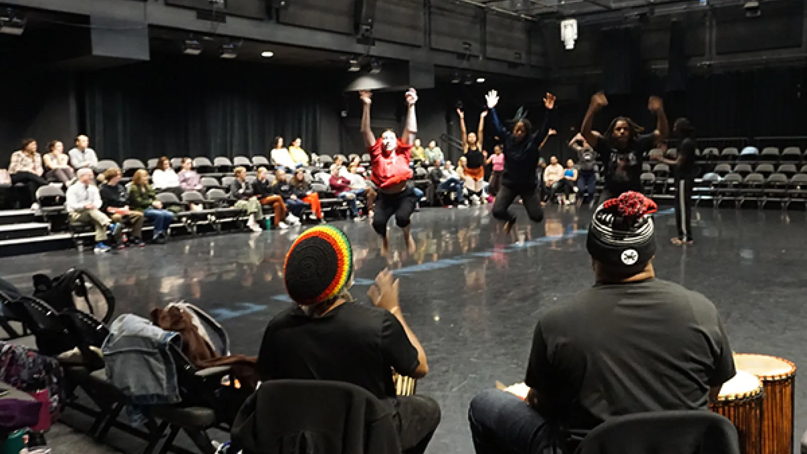 dancers jumping in front of drummers in a theatre