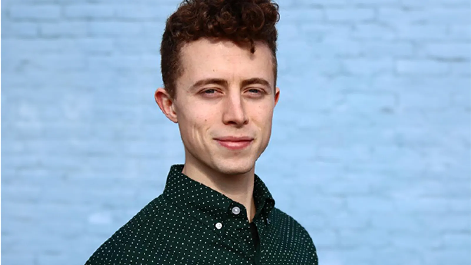 person with short curly brown hair wearing black shirt with white polka dots