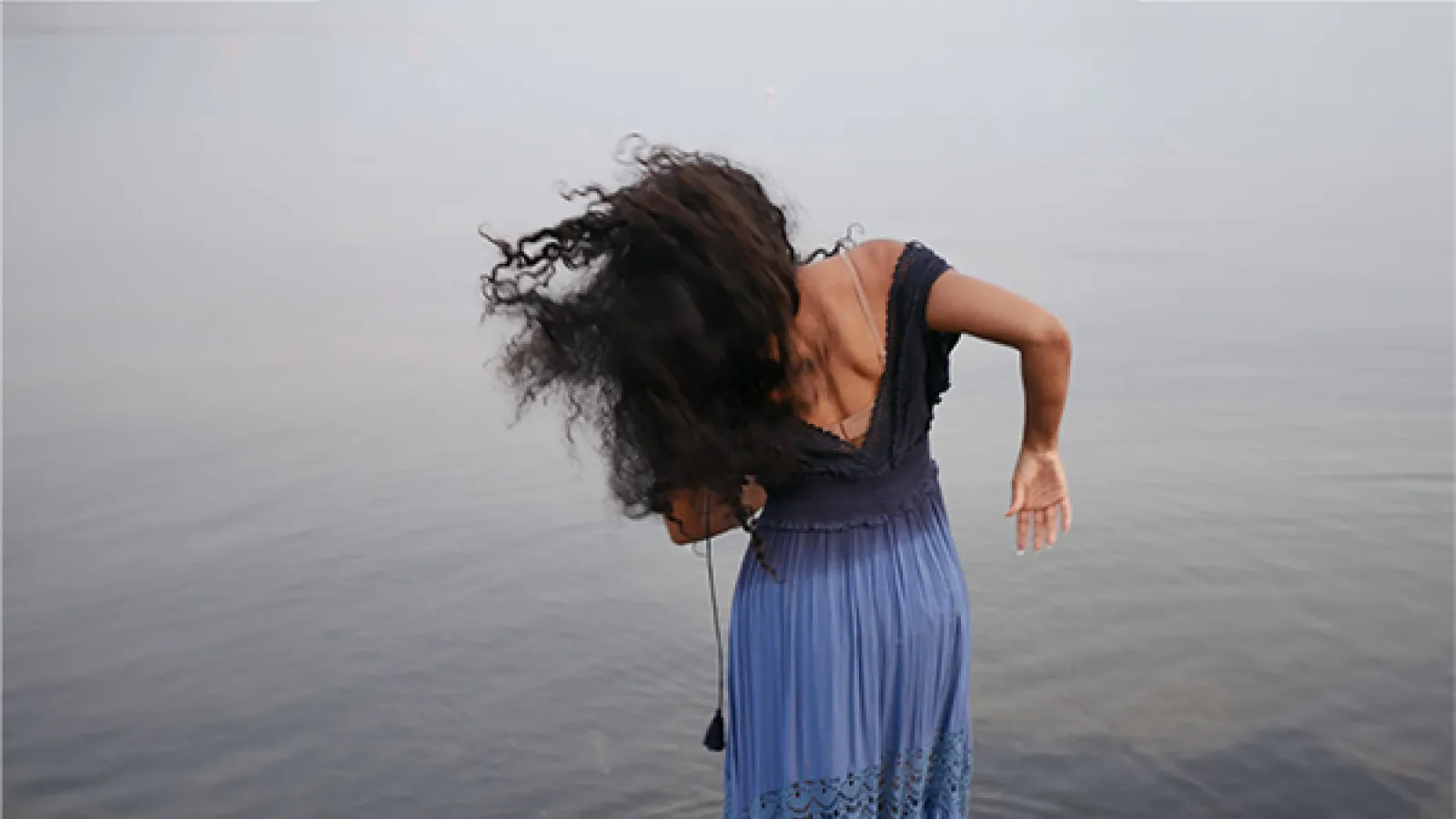 woman with black hair wearing blue dress standing in water