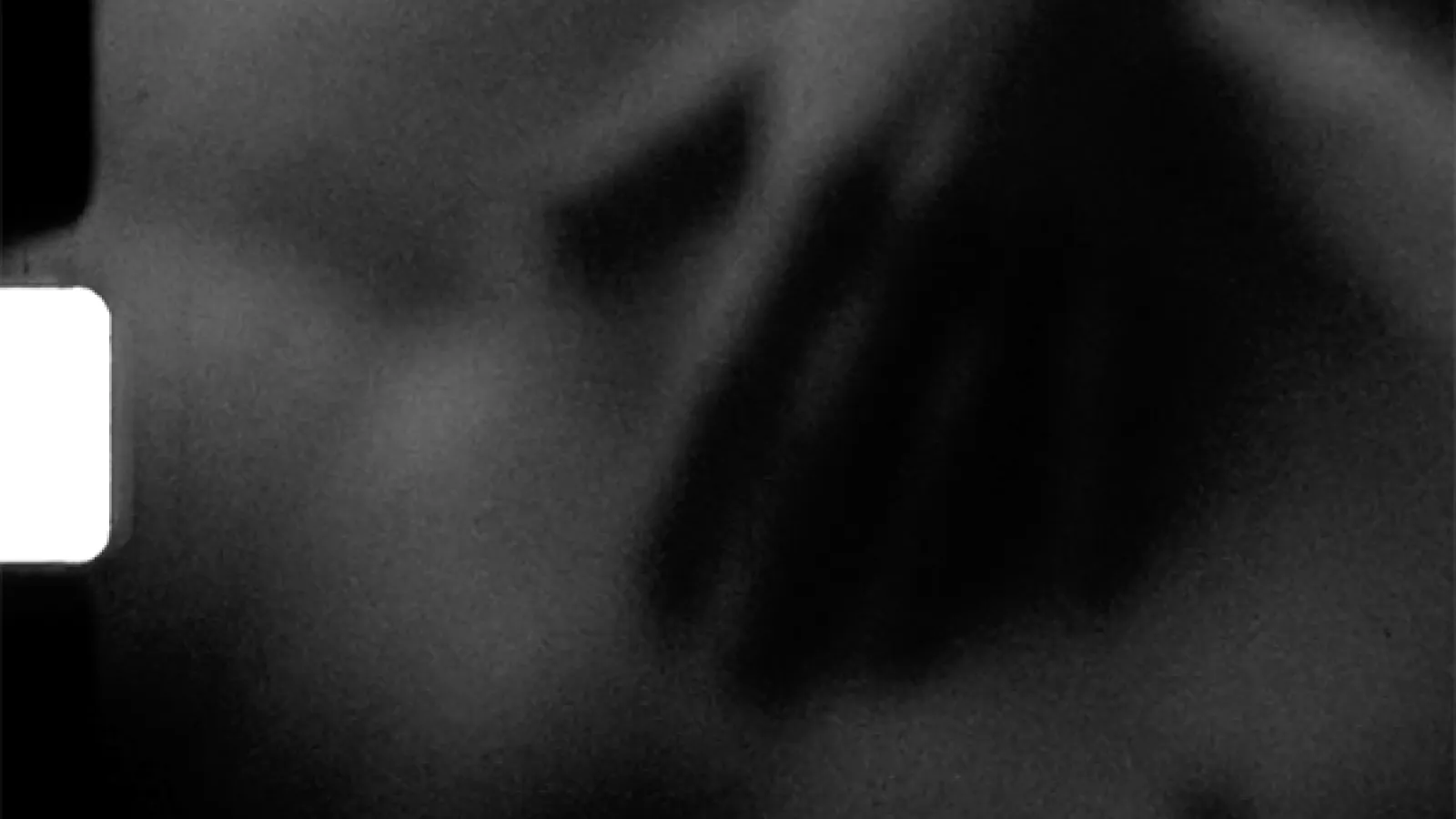 Abstract black-and-white image with soft, blurred shadows across a grainy surface; a torso with a hand over their stomach.