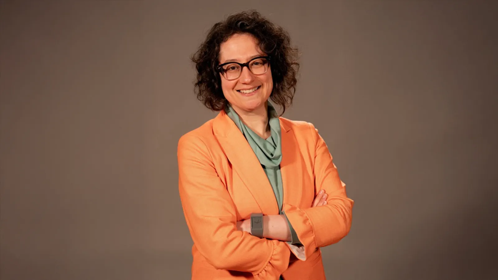 Woman with short curly brown hair wearing glasses and smiling