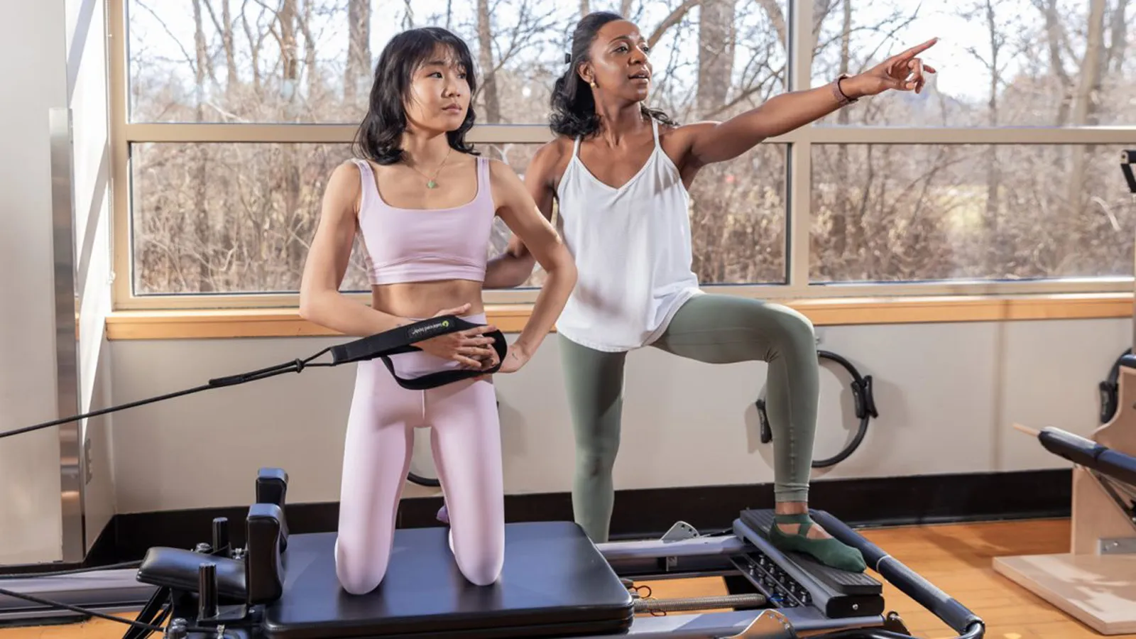 A woman on the left exercising guided by a woman on the right