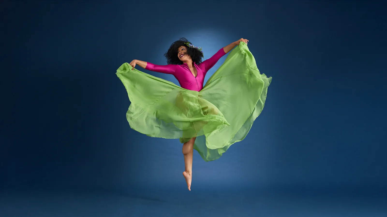 Woman wearing pink top and green skirt leaping