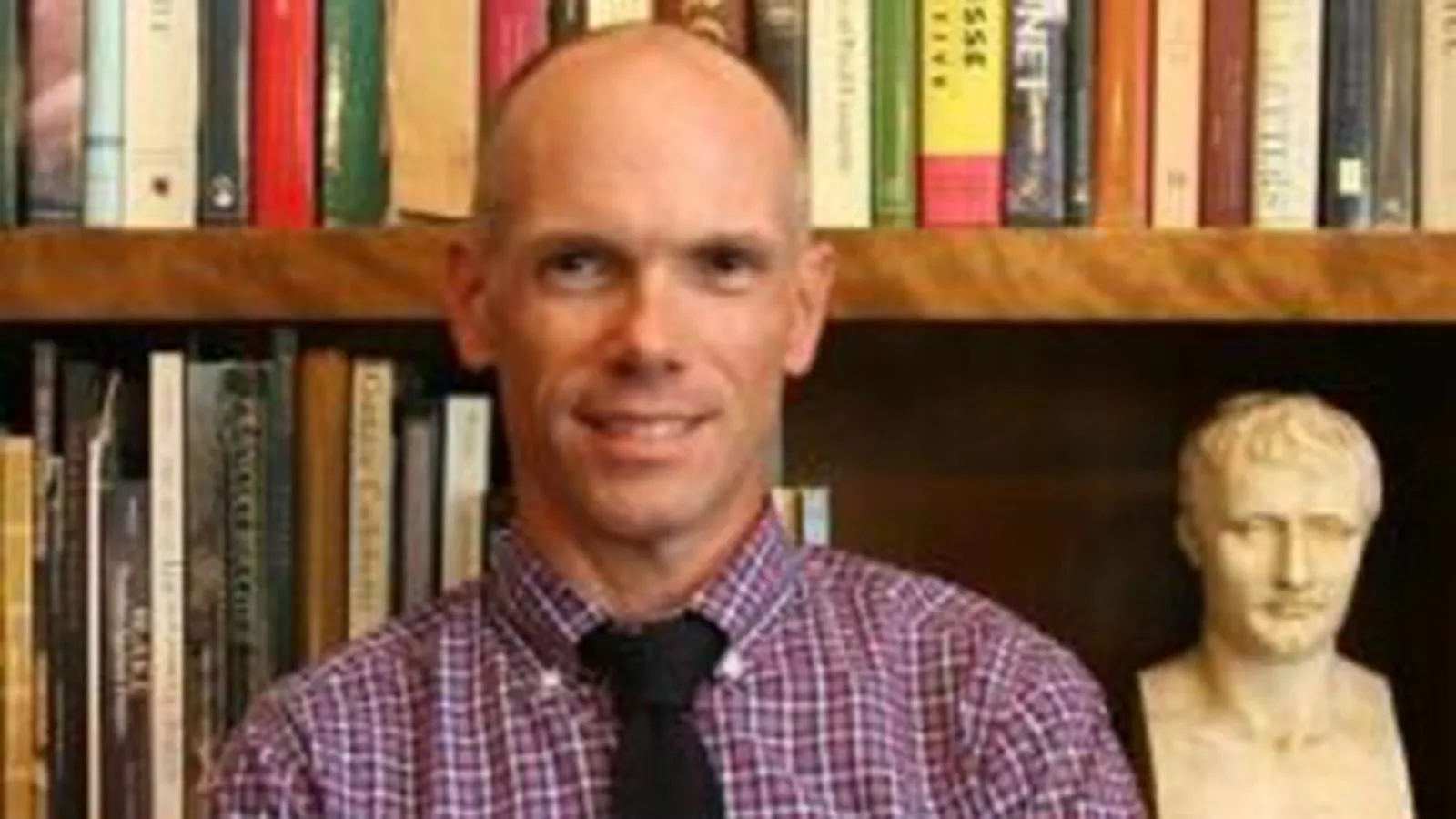 A headshot of a man standing in front of a bookshelf 