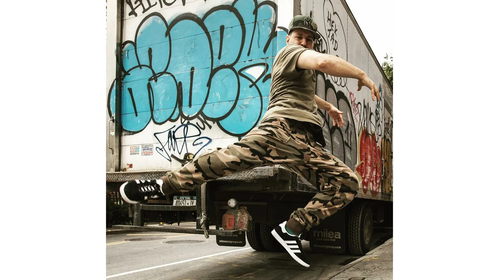 dancer jumping in front of a box truck covered with graffiti 