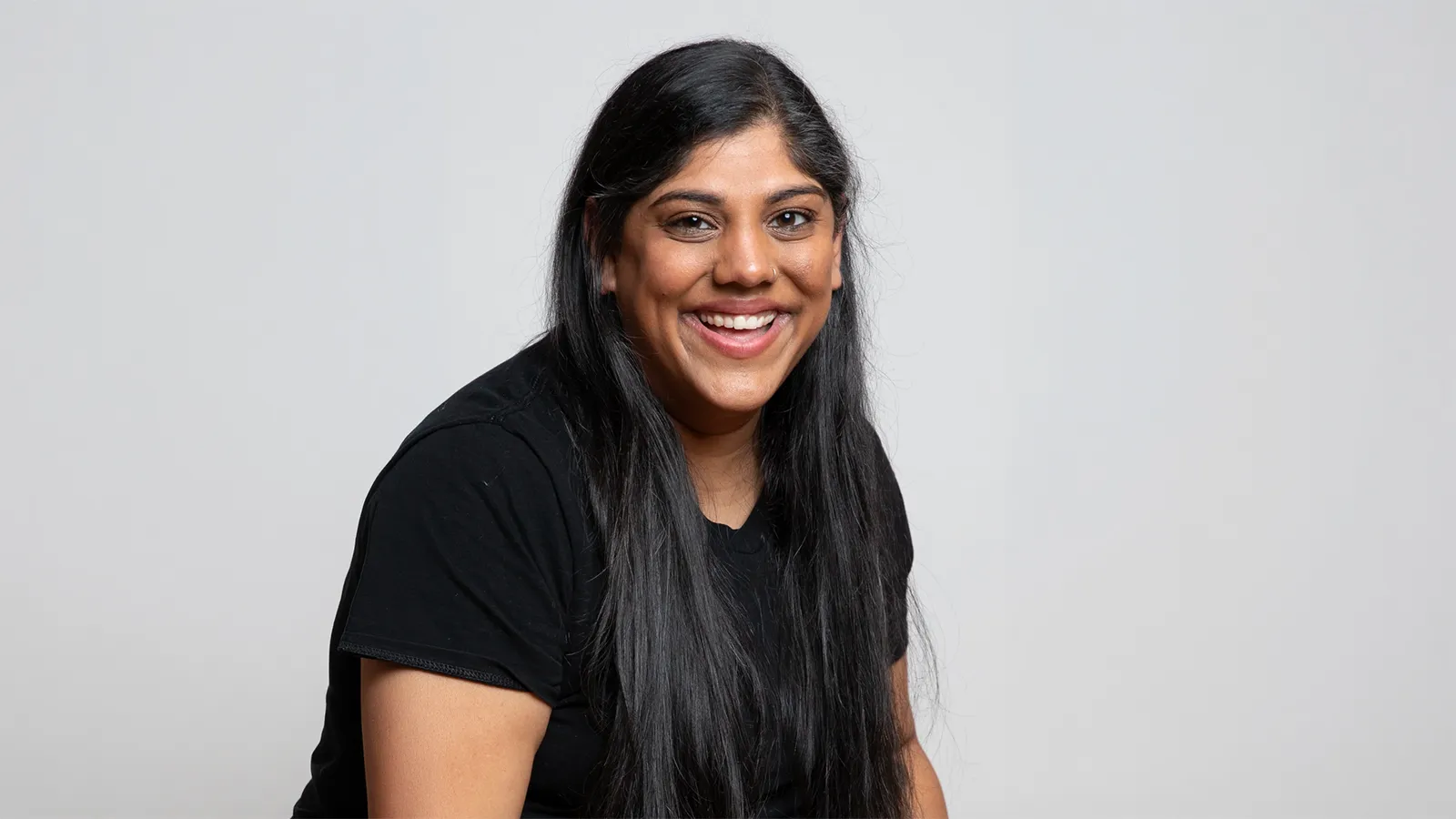 Person with long black hair in short sleeve black shirt in front of white background
