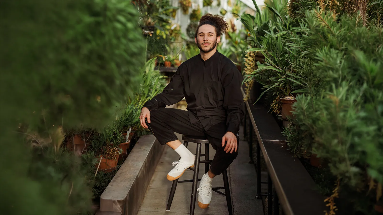 Person sitting on stool surrounded by plants