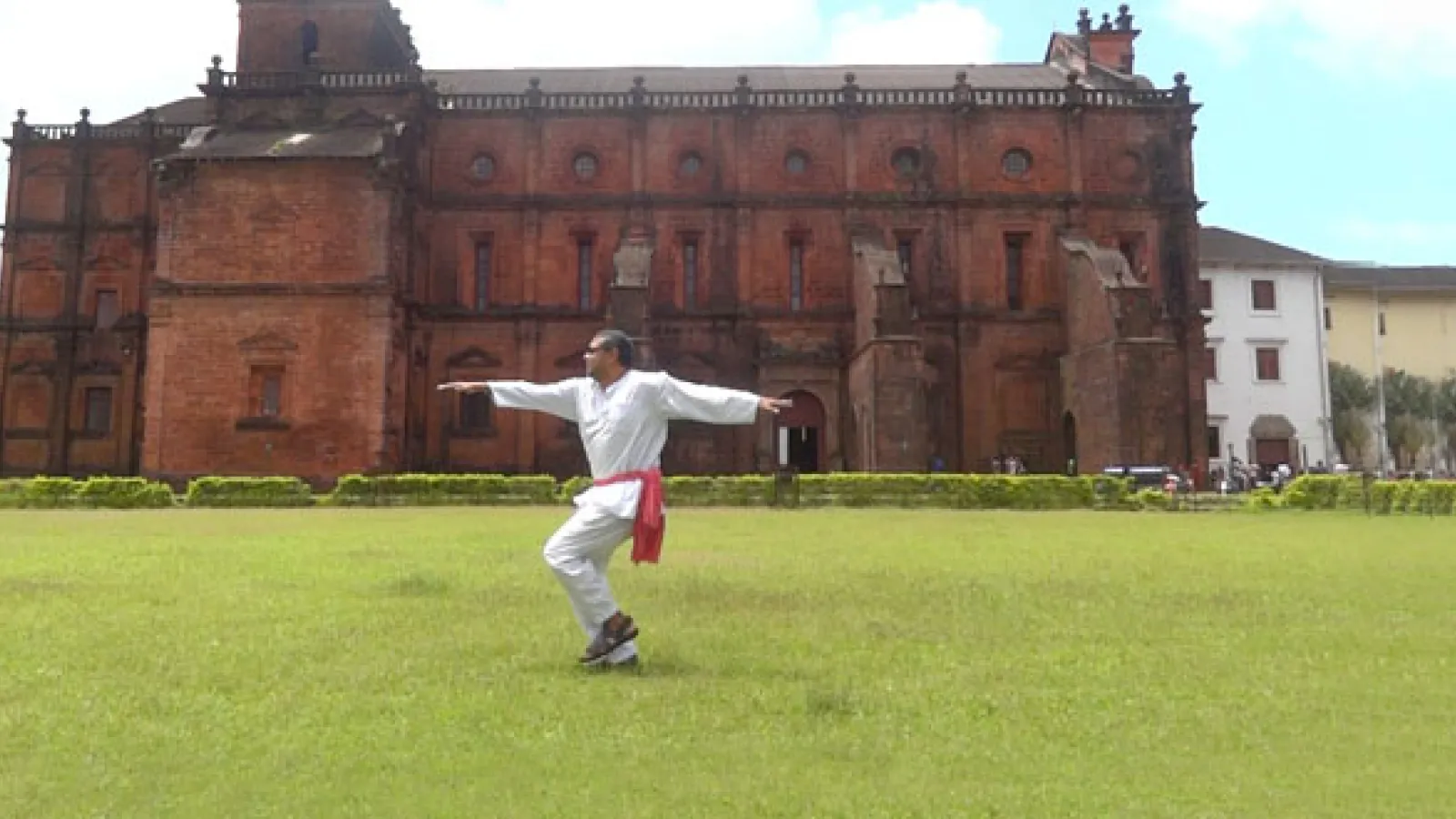 A man holds his arms out for a pose on the grass in front of an enormous old mansion.