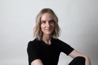 A person with blonde hair and a black shirt sitting in front of white background