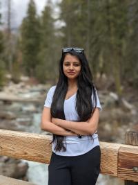 Person with long black hair standing in front of woods