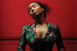 Person with eyes closed wearing green patterned dress in front of red background