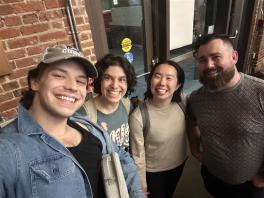 Four people posing for a photo in front of a brick wall