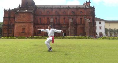 A still from the video Globe Trot. A man holds his arms out for a pose on the grass in front of an enormous old mansion.