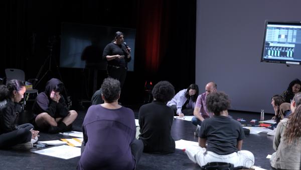 a person speaking to a people sitting on the floor