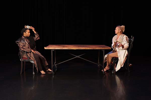 Two dancers seated at a table on a stage. 