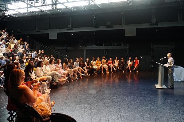 Students seated on stage listening to a speaker