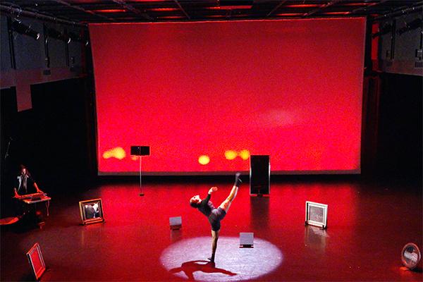 Musician and dancer performing on stage with red lit background