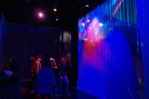 Audience looking at digital image on white scrim in dark room