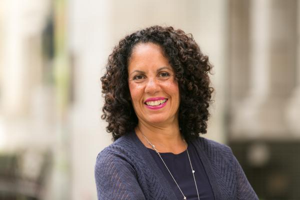 Woman with curly dark brown hair wearing blue shirt in front of blurred background