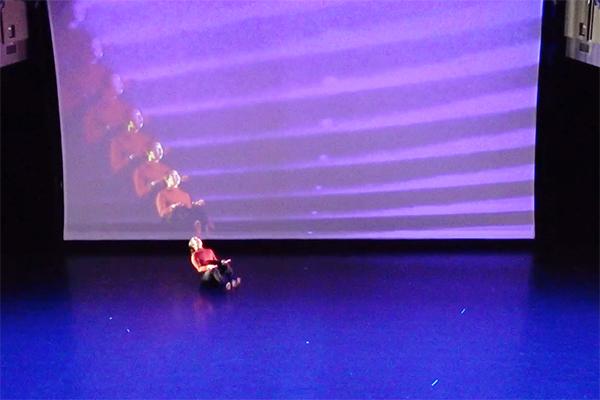 Dancer sitting on floor in front of screen with her image projected multiple times.