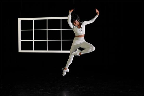 Dancer dressed in white leaping in front of white window frame