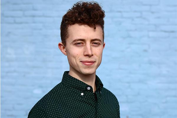 person with short curly brown hair wearing black shirt with white polka dots