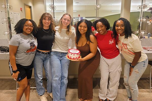 A group of people standing in front of a mirror with a cake