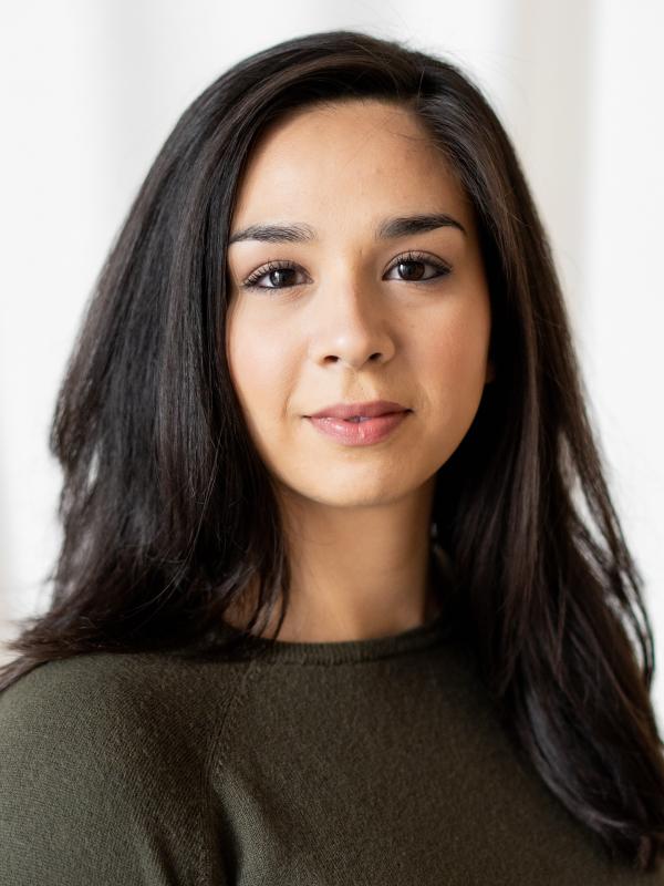 Woman with medium length dark brown hair, and an olive green sweater in front of a white background