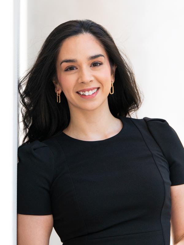 Woman with dark brown and gold earrings wearing a black dress in front of a white background