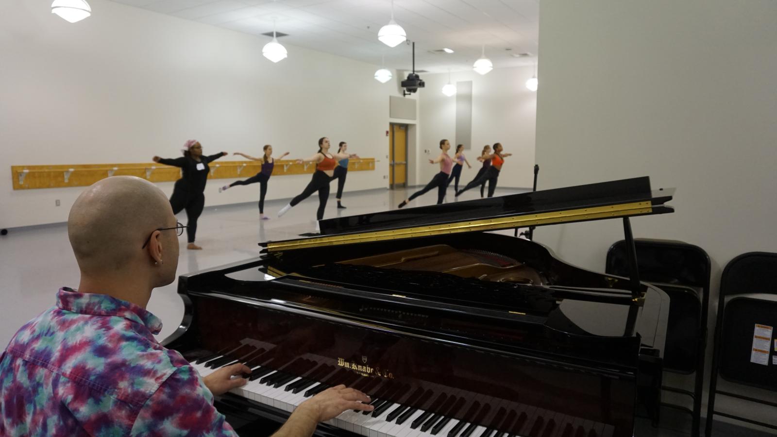 Accompanist playing piano while dancers rehearse in studio