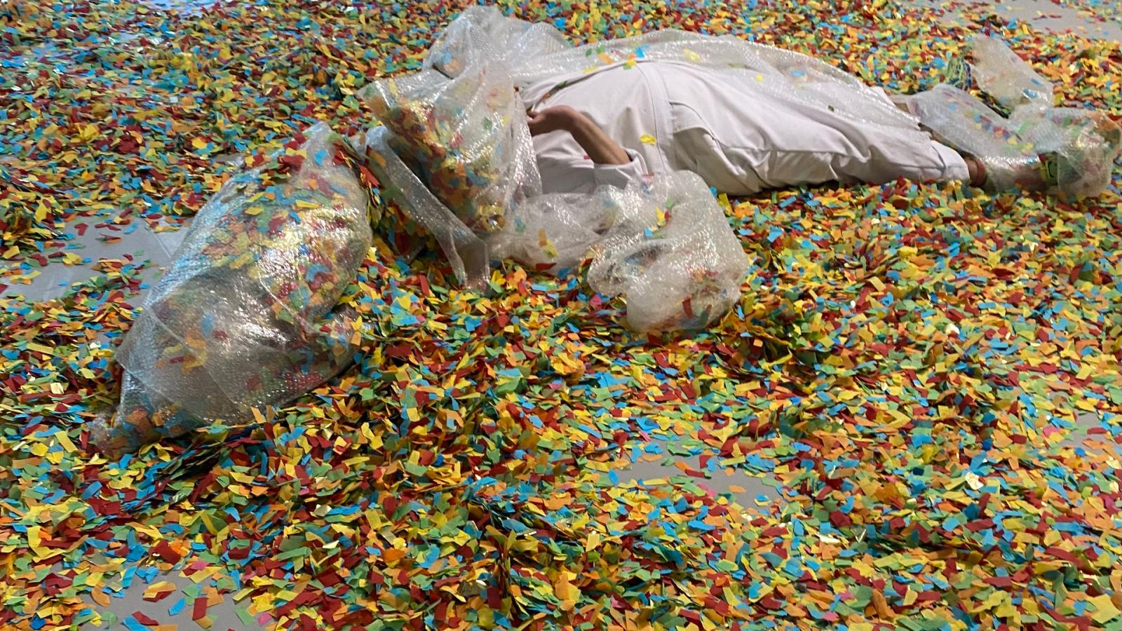 man wrapped in plastic and covered with confetti