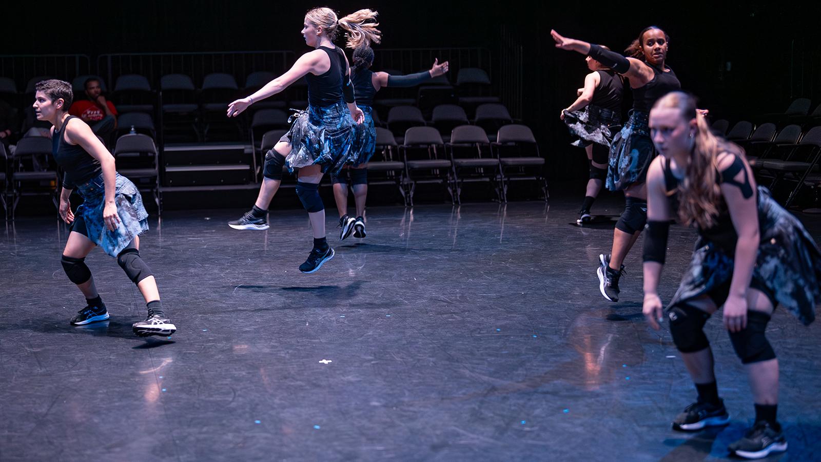 dancers wearing kilts and black tank tops on a lit stage