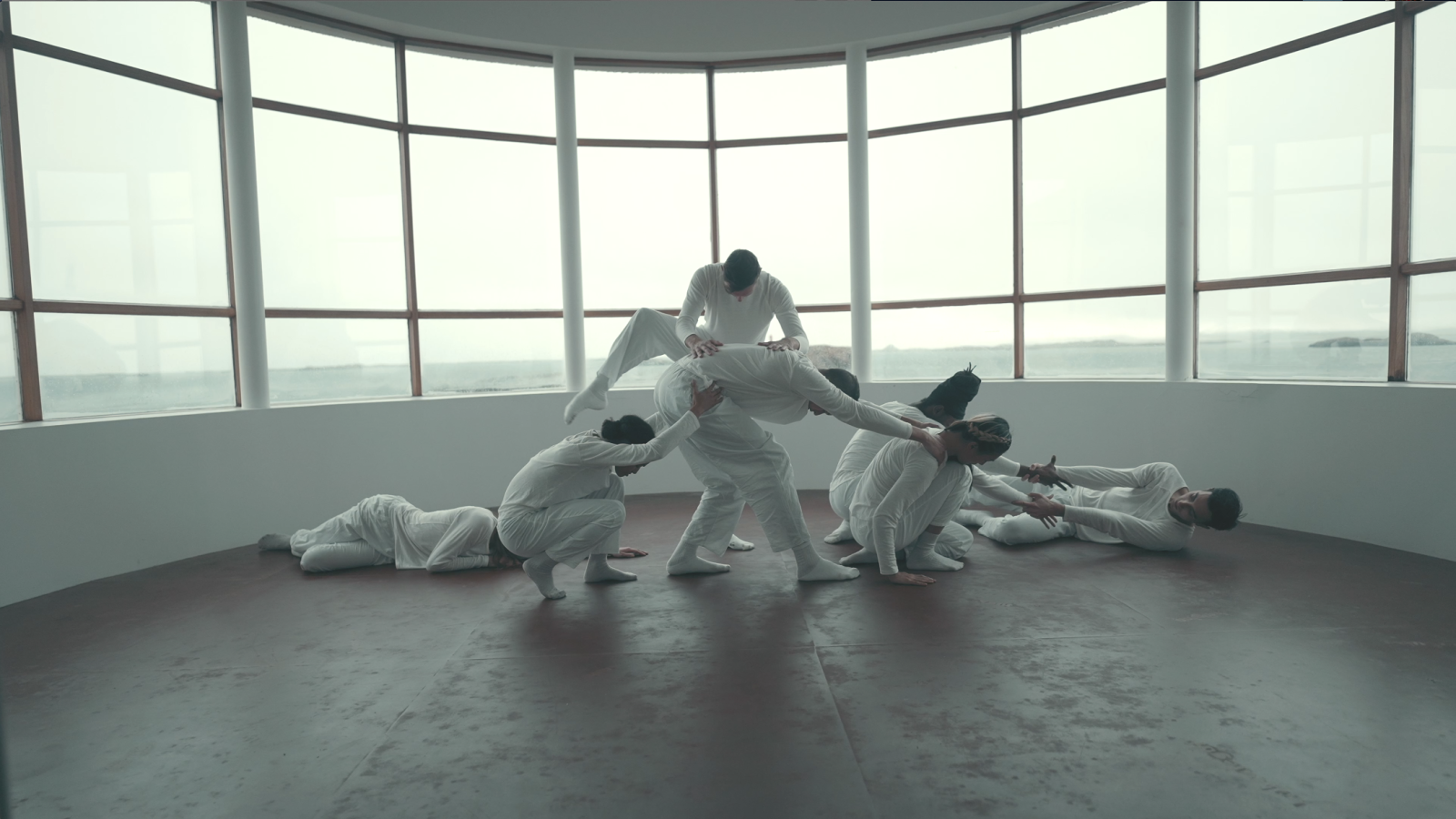 Dancers dressed in white in front of a large window