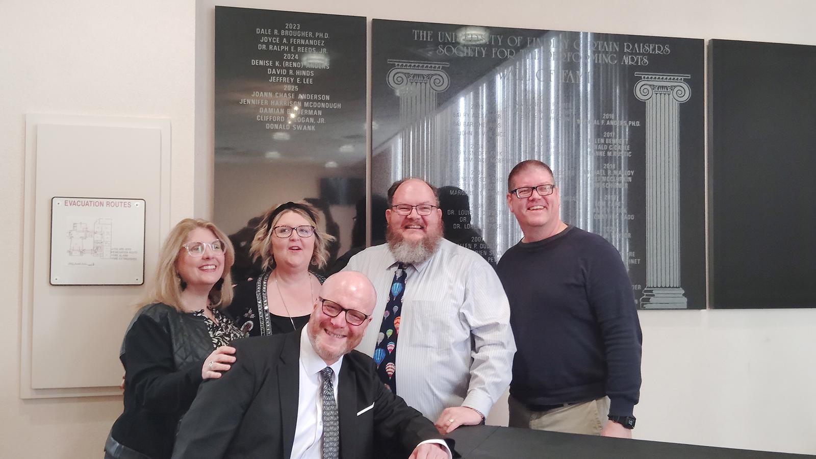 5 people standing in front of wall with names inscribed on it