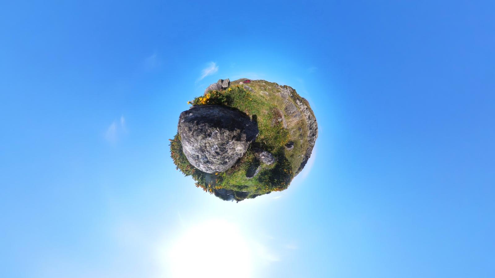 A 360 image of a green landscape that has been animated to be a circle in the middle of the frame. Bright blue sky surrounds the landscape orb.