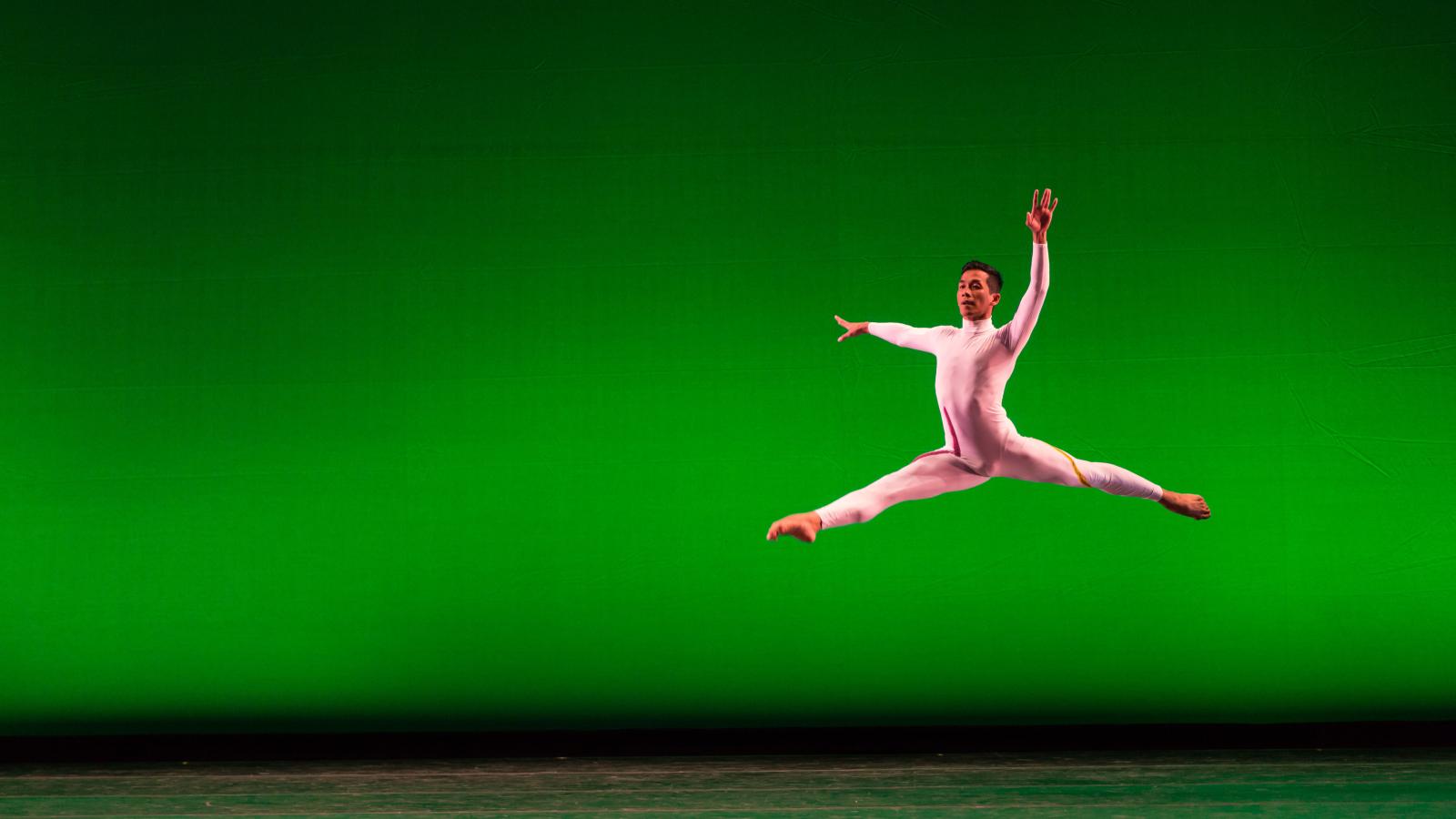 Dancer in modern white costume leaping in front of green background