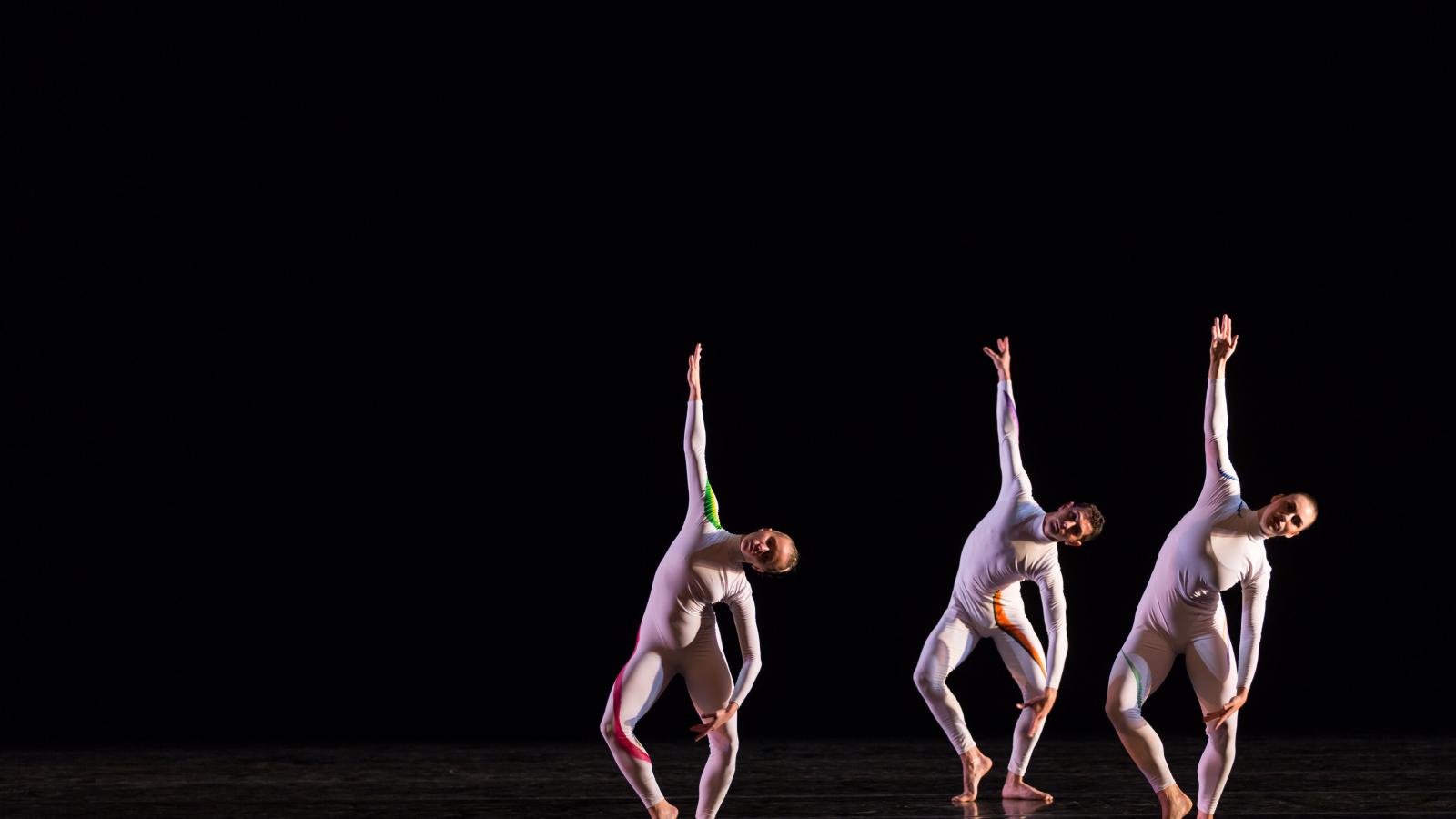 Three dancers in modern white costumes dancing in front of black background