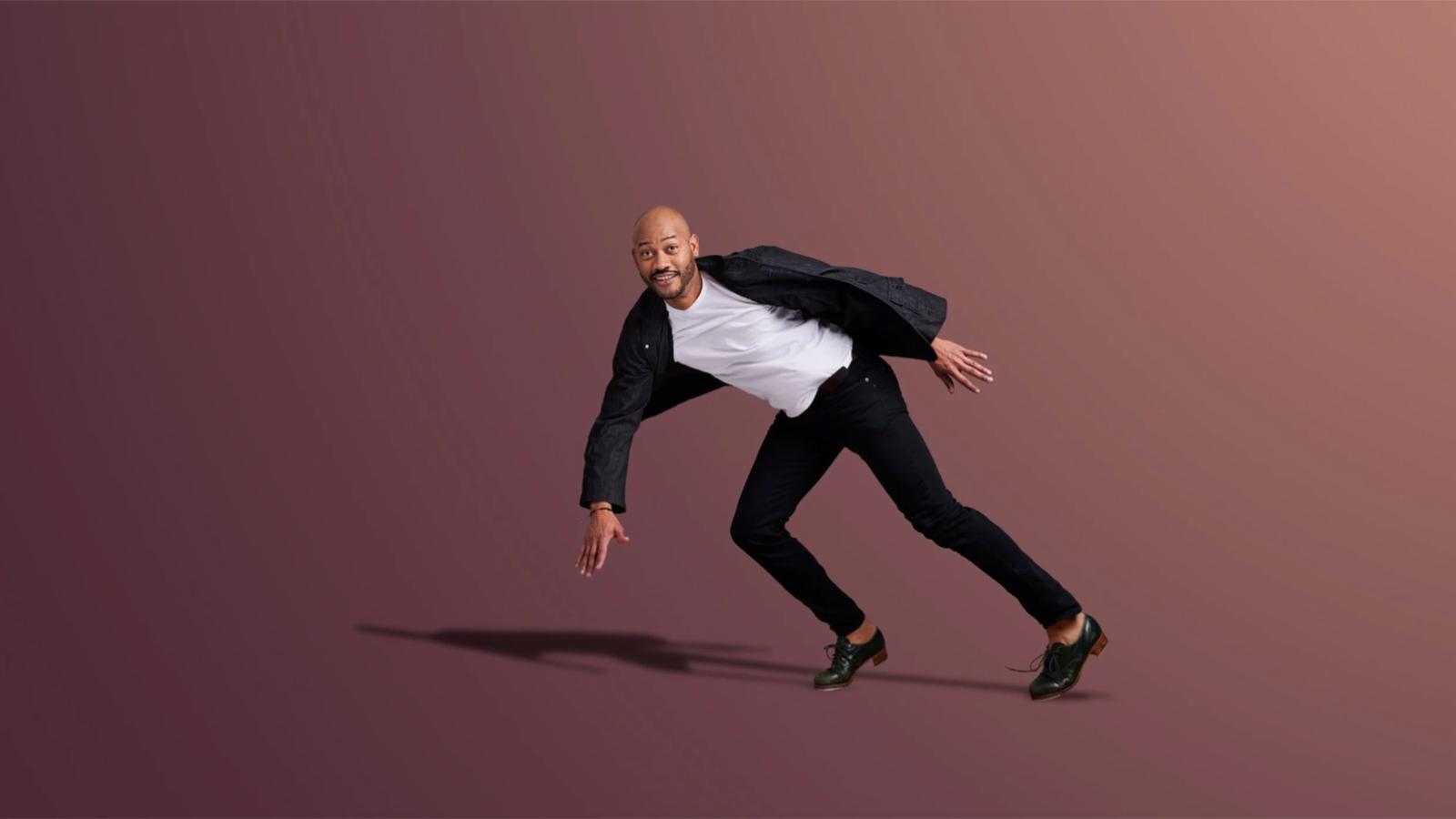 man wearing white shirt under black shirt with black pants and tap dance shoes leaning to the left