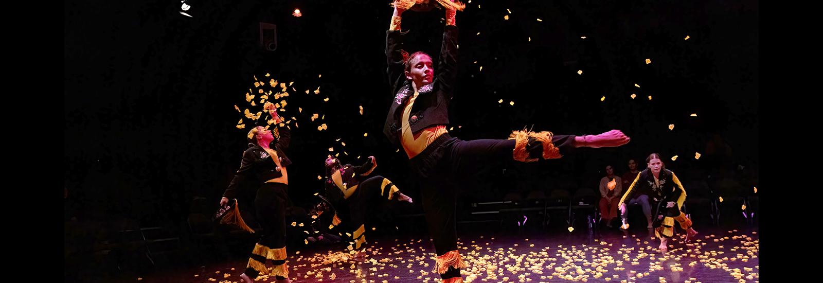 Dancers performing on a stage with orange flower petals falling 