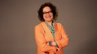 Woman with short curly brown hair wearing glasses and smiling