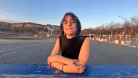 a person sitting on a blue picnic table outdoors with blue sky, buildings, and people in the background